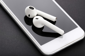 White wireless earphones with mobile phone on black background - obrazy, fototapety, plakaty