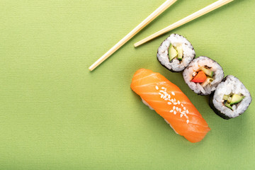 Sushi salmon nigiri and cucumber roll with chopsticks on a green background, top view