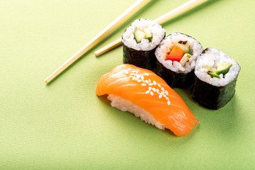 Sushi salmon nigiri and cucumber roll with chopsticks on a green background