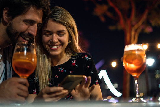 Smiling young couple using smartphone while having drink at outdoor cafe - Powered by Adobe