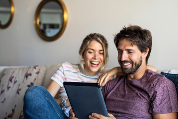 Smiling young couple using digital tablet while relaxing on sofa at home