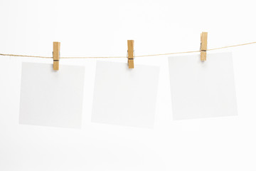 Empty paper sheets for notes, frames that hang on a rope with clothespins and isolated on white. Blank cards on rope. Mockup template for memories backdrop, photos, social media etc.