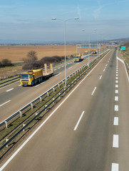 Yellow transportation semi trucks in line as a caravan or convoy on a countryside highway under a blue   sky