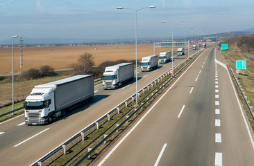 Convoy of many White transportation  trucks in line as a caravan or convoy on a countryside highway under a blue sky