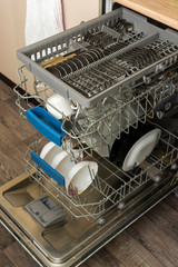 Clean plates, cups, spoons and forks in a dishwasher at home kitchen