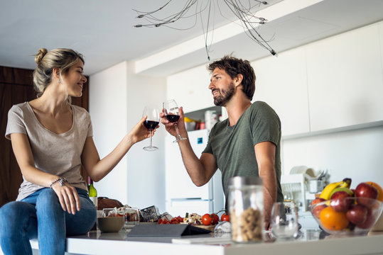 Smiling couple toasting wine glasses in kitchen while standing in kitchen