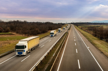 Convoy or caravan of transportation trucks on a highway on a bright blue day. Highway transportation with lorry tracks