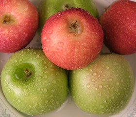 red and green apples in drops of water on a plate