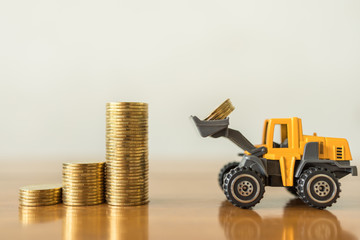Business, Money,  Finance and Saving  Concept. Close up of miniature mini loader truck contain 4 coins and puting to top of stack of gold coins on wooden table with copy space.