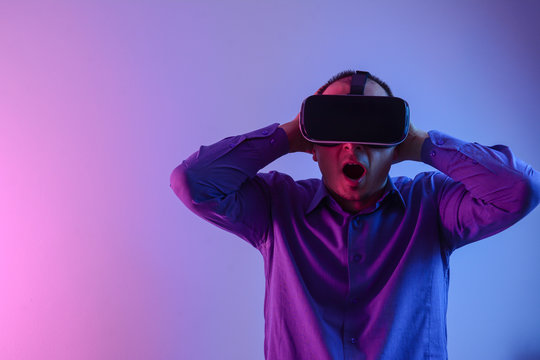 Man wearing virtual reality goggles. Studio shot, neon light background. Portrait of amazed excited man watching virtual reality glasses with open mouth expression over neon background