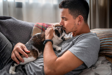 Primer plano de hombre joven besando la cabeza de un gato blanco y marron de ojos azules