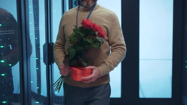 Male engineer with present and flowers walking along server cabinet corridor. Happy young woman receiving suprise on Valentine's day feel shy smile cheerful talking together at data center.