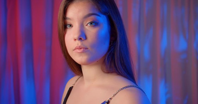 Portrait caucasian beautiful confident girl neon light look at camera bare shoulders shine radiance background profile view blue light