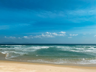 Fototapeta na wymiar Sandy seashore, calm soft waves at sea, sunny weather, blue sky with white clouds