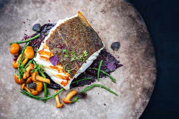 Gourmet fried European skrei cod fish filet with glasswort, fungi and algae as top view on a modern...
