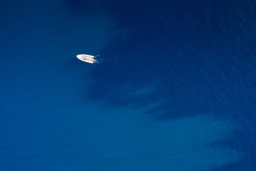 Fototapeta na wymiar White small motor boat is in the middle of the sea with the turquoise blue water. Dark blue and blue water divides the sea in two parts.
