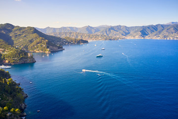 Obraz premium Arial view on yachts and boats, sailing in the Ligurian Sea on the mountain background, Portofino, Italy. Rocks and hills seaside with the traditional Italian houses on the top.