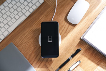 Smartphone charging with wireless pad, flat lay. Modern workplace - obrazy, fototapety, plakaty