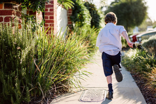 Boy in a school uniform running along a path after school