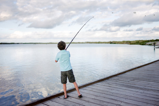 Child casting a line from a fishing rod off a dock at a river mo