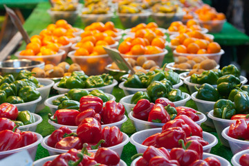 Red and green peppers and fruits for sale in bowls on a market stall.