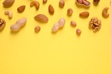 Different delicious nuts on yellow background, flat lay. Space for text