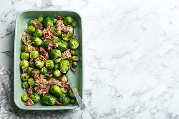 Delicious Brussels sprouts with bacon on white marble table, top view. Space for text