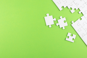 top view of white blank unfinished jigsaw puzzle on green background, completing a task or solving a problem concept