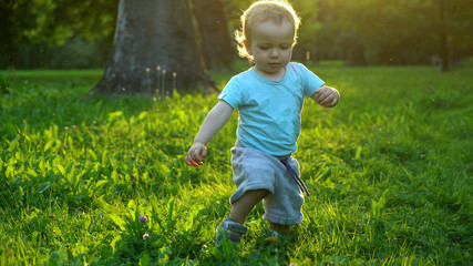 Cute baby boy making first steps in sunset lights