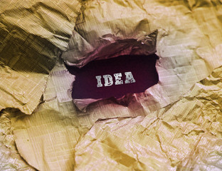 Torn golden foil paper with word Idea behind it. Business idea concept