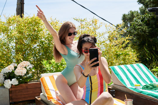Content women in swimsuits taking selfie on terrace