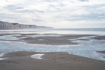 Falaises de Caux. Somme. la plage de sable est à marée basse. Des nappes d'eau se sont formées sur la plage. Le ciel nuageux se reflete dans ces flaques d'eau. Les falaises en craie à l'infini