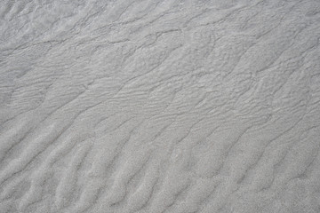 Fototapeta na wymiar Gros plan sur des mini dunes de sable gris sur une plage à marée basse, ondulations sablonneuse.s