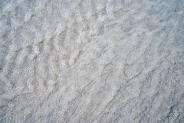 Gros plan sur des mini dunes de sable gris sur une plage à marée basse, ondulations sablonneuse.