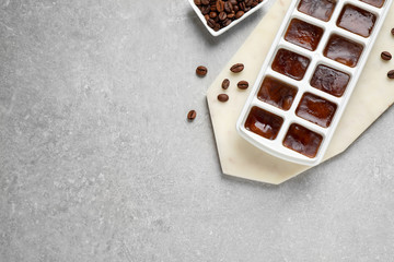 Ice cubes with coffee beans in tray on grey table, flat lay. Space for text
