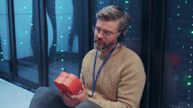 Desperate bearded IT admin caucasian man in frustration hugging tight a present box from valentine regretting thinking while staying at server room database.