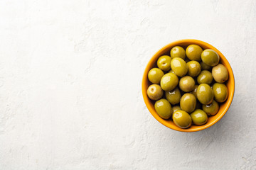 Green olives in ceramic bowl on concrete background. Top view, copy space.