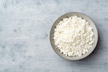 Cottage cheese in bowl on concrete background. Top view, copy space.