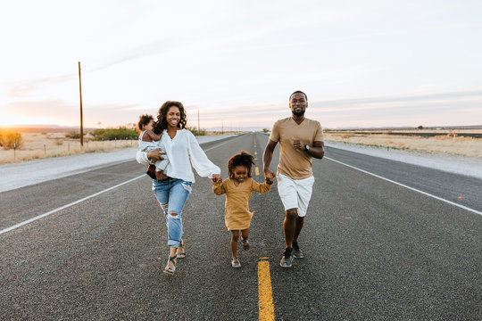 Portrait of smiling family walking on tarmac road during sunrise