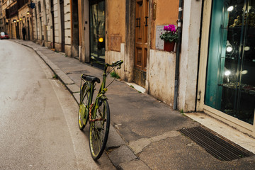 There is a green bicycle standing on the street. Cozy narrow street in Italy. 