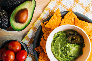 Guacamole bowl with nachos on vintage wooden table with fresh ingredients around it. Copy space. Vegan food