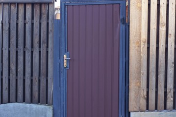 one brown closed metal door and a wooden fence wall on the street