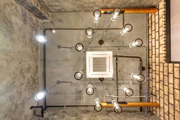 looking up on gray concrete ceiling with halogen spots and edison lamps in loft office room with air conditioning and orange ventilation pipe