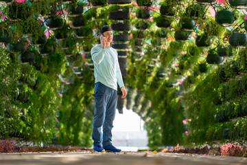 Man talking by cell phone in the colourful floral and umbrella arch at the Corniche Station. Doha, Qatar