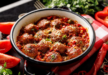 Meatballs in tomato sauce with the addition of aromatic herbs and cheese in an enamel dish top view
