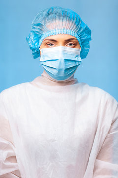 female doctor in medical uniform portrait, in a cap and a protective mask on her face. Blue background. Surgeon before a surgery.