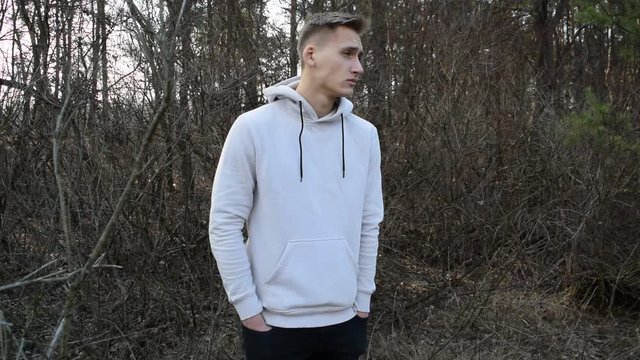 A young man in a white jacket stands against the gray nature of dry branches