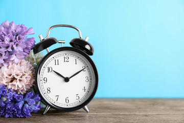 Black alarm clock and spring flowers on light blue background, space for text. Time change