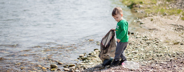 Save environment concept, a little boy collecting garbage and plastic bottles on the beach to dumped into the trash.