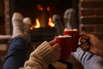 Couple with cups of delicious cocoa resting near fireplace at home, closeup. Winter vacation